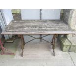 A cast iron garden table with scrolled supports, beneath a weathered teak slatted rectangular top,