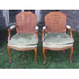 A pair of pale beechwood open armchairs in the French manner, with cane panelled backs, loose