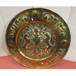 A large embossed brass wall charger with heraldic panel, lion unicorn helmet, shield, etc, in a