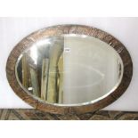 An oval Arts & Crafts style wall mirror with bevelled edge plate within a planished copper clad