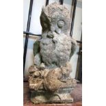 A weathered composition stone garden ornament in the form of an owl clutching its prey, raised on