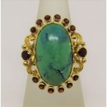 Yellow metal cocktail ring set with cabochon turquoise within a surround of circular garnets, size