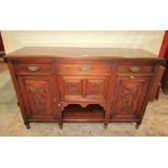 An Edwardian walnut sideboard enclosed by an arrangement of cupboards and drawers with carved