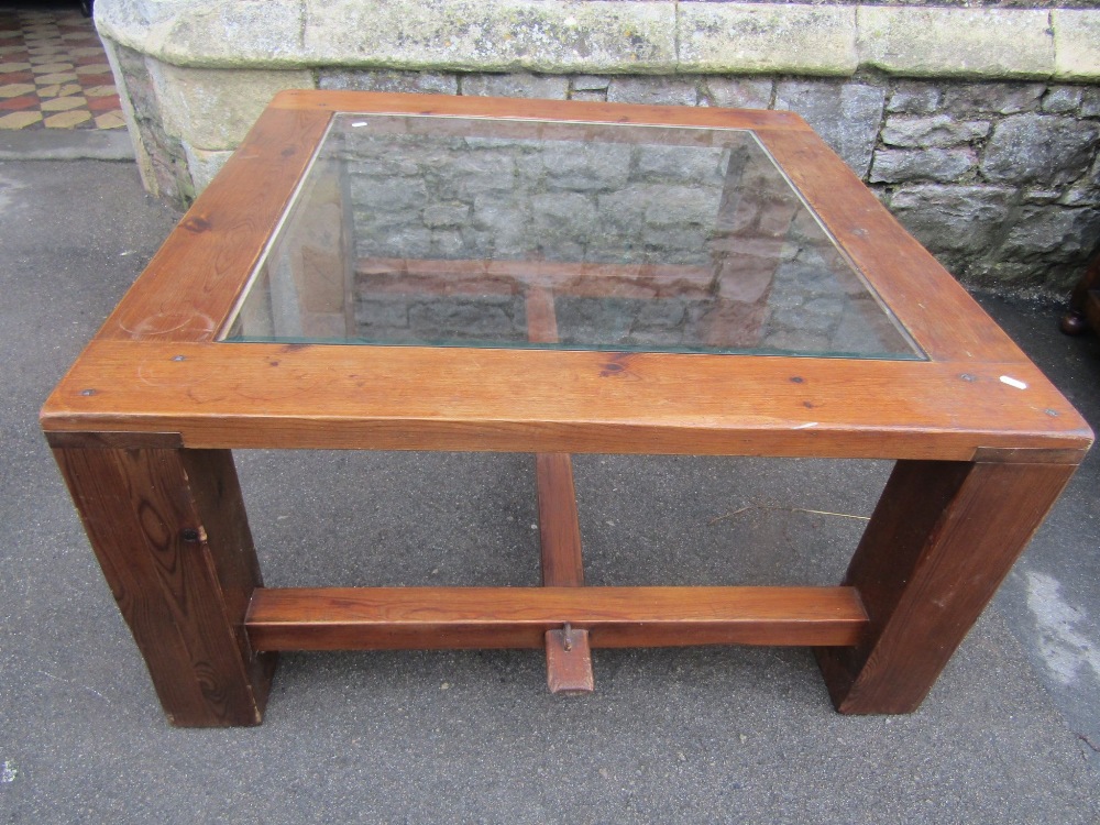 A sturdy pine framed occasional table of square form with inset glass panel raised on substantial