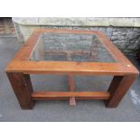 A sturdy pine framed occasional table of square form with inset glass panel raised on substantial