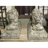 A pair of weathered composition stone garden ornaments in the form of recumbent lions, clutching