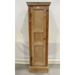 A narrow stripped pine floorstanding side cupboard enclosed by a full length moulded triple panelled