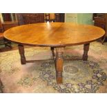 A large circular oak dining table, the heavy plank top raised on four square cut supports, united by
