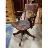 An Edwardian/1920s swivel office desk chair, the stained beechwood frame with upholstered pad seat