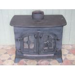 A cast iron wood burning stove enclosed by a pair of arched and glazed quarter panelled doors (