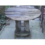 A rustic weathered oak, or possibly elm, garden table, of circular form raised on shaped and