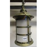A brass hall/porch lantern of cylindrical form with strap work frame and frosted shade