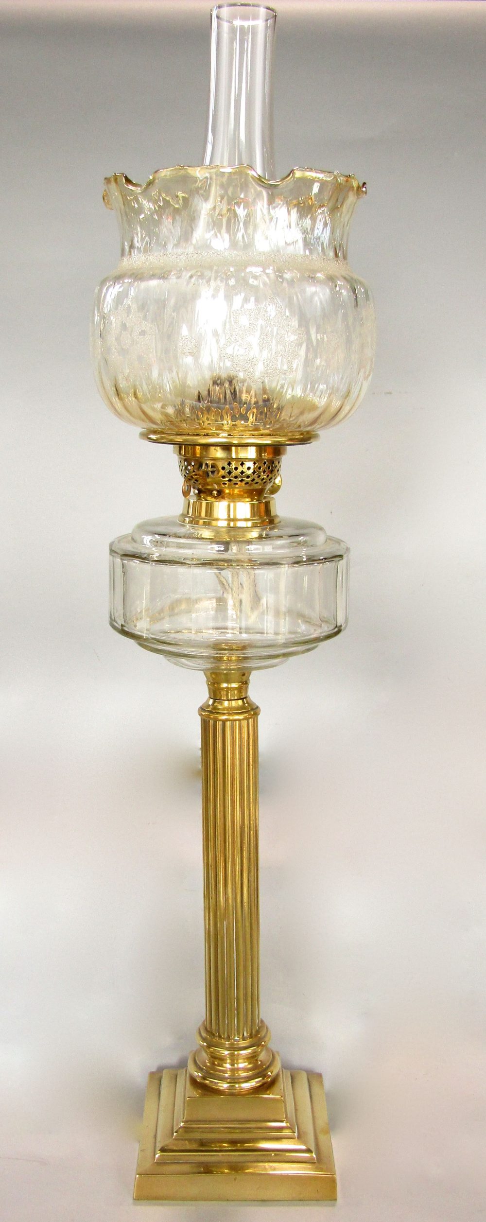 A brass table standing oil lamp, the reeded column on a stepped frame with moulded glass font,