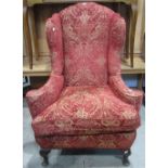 A Georgian style wing armchair with shaped outline, well pronounced swept and rolled arms, with