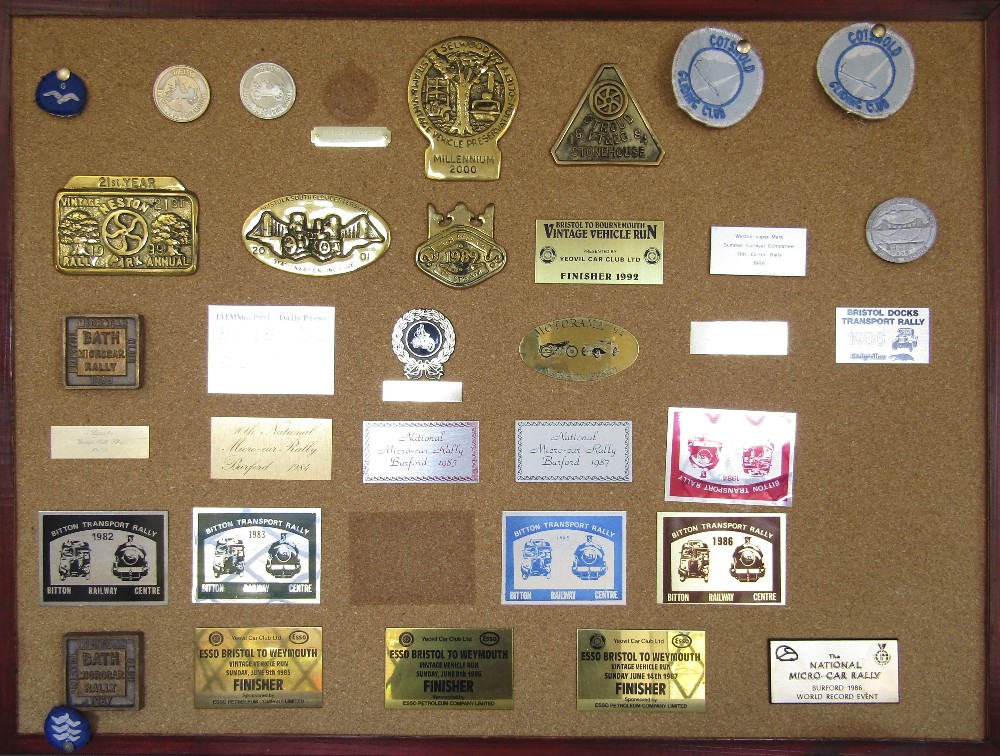 A cork board displaying a number of vintage transport rally plaques, circa 1980/2000