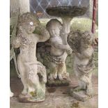 A weathered cast composition stone bird bath in the form of a standing cherub clutching a cornucopia