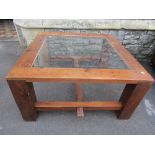 A sturdy pine framed occasional table of square form with inset glass panel, raised on substantial