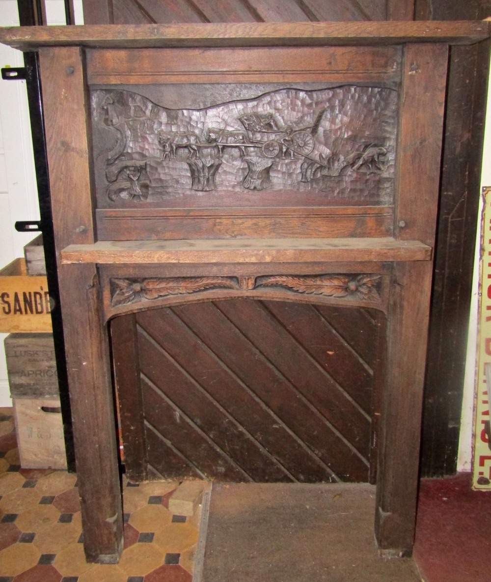 A substantial oak fire surround with pegged frame, the raised back with carved panel of a harvesting