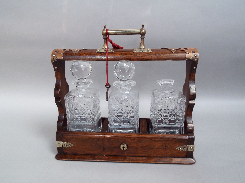 An early 20th century oak and brass mounted tantalus of usual form fitted with three square cut