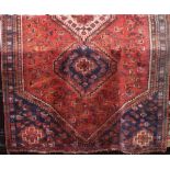 Middle Eastern rug with three central medallions framed by further Paisley scrolls upon a washed red