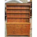 A narrow stripped pine kitchen dresser, the base enclosed by three panelled doors beneath three