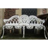 A cream painted cast aluminium garden bench with shaped outline and decorative pierced foliate