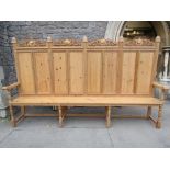 A large stripped and waxed pine settle, the raised moulded panelled back with deep relief