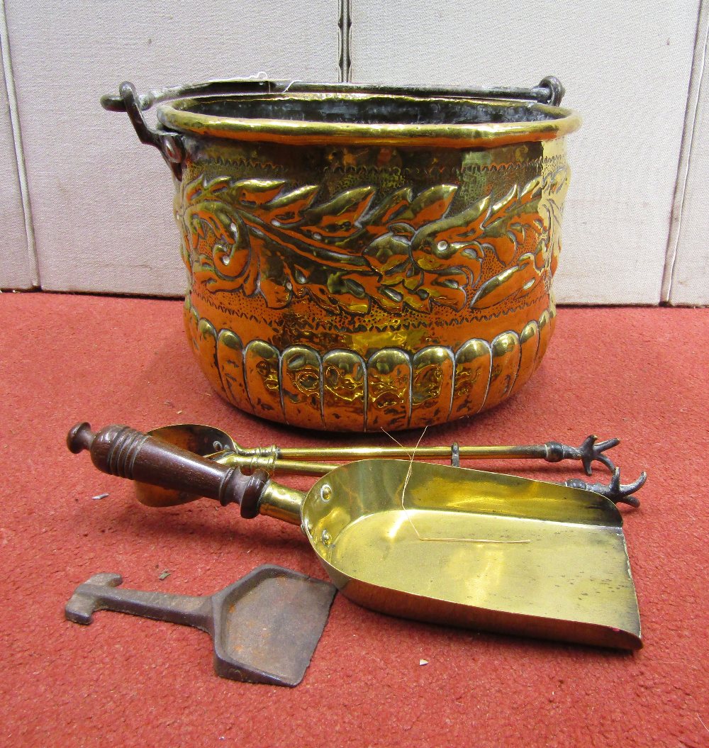 An antique embossed brass cauldron of circular form with steel loop handle, with trailing floral and
