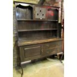 An Edwardian/1920s dark stained oak dresser, the recessed upper section with open shelves,