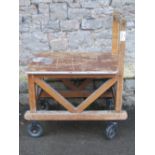 A sturdy ex ministry oak framed trolley with turned handle, flat bed and substantial castors, approx