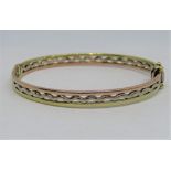 9ct tri-colour hinged bangle of wavy openwork design, 12.6g, within an antique bangle case
