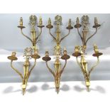 Set of six gilt cast metal twin branch wall lights with ribbon back plates and fluted scrolled arms,