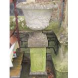 A weathered composition stone garden urn of circular waisted form with flared rim, repeating