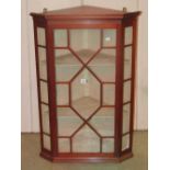 A small Georgian style hanging corner cabinet enclosed by an astragal glazed panelled door revealing
