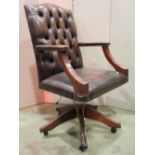 A reproduction swivel desk chair, with faux brown leather upholstered seat, button back and arms,