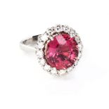 A TOURMALINE AND DIAMOND RING claw-set to the centre with an oval mixed-cut orangey pink