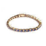 A SAPPHIRE AND DIAMOND TENNIS BRACELET 30 claw-set oval mix-cut graduating blue sapphires,