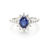 A SAPPHIRE AND DIAMOND RING stylised as a flowerhead, centred by a claw-set oval mixed-cut sapphire,