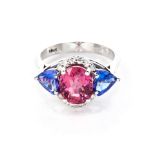 A TOURMALINE, TANZANITE AND DIAMOND RING claw-set to the centre with an oval mixed-cut pink