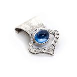 A SAPPHIRE AND DIAMOND ENHANCER centred by an oval cabochon tube-set sapphire, in an openwork