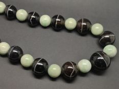 Single row of graduated jade and onyx beads, with yellow metal tongue but no clasp, total length