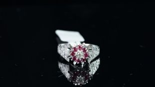 A ruby and diamond cluster ring, centring a round brilliant cut diamond, illusion set, surrounded by