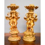 A pair of gold painted candlesticks, modelled with cherubs and having cut glass drops, 24cm high.