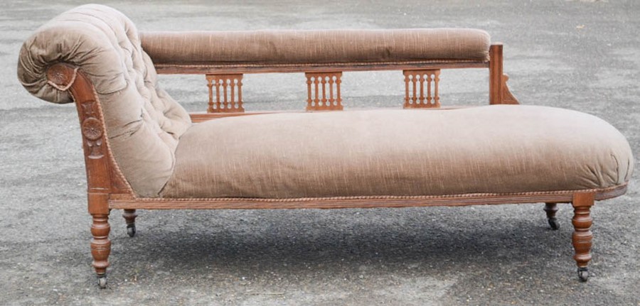 An Edwardian chaise longue, the frame carved with decoration, and having a buttoned velour