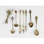 A group of white metal pickle forks, spoons and other commemorative spoons.