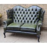 A green leather camel back settee, two seater with buttoned back.150cm wide, 110.3cm tall, 85cm