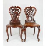 A pair of Victorian mahogany hall chairs, with pierced and shaped foliate backs, raised on two