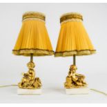 A pair of French table lamps, in the form of gilded cherubs raised on white marble bases, with