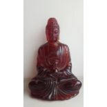A Chinese cherry amber Buddha sitting in the lotus position.19cm high, and 703g.