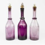 Three Bohemian purple glass wine bottles with cork and metal stoppers cast with grape and vine, 33cm